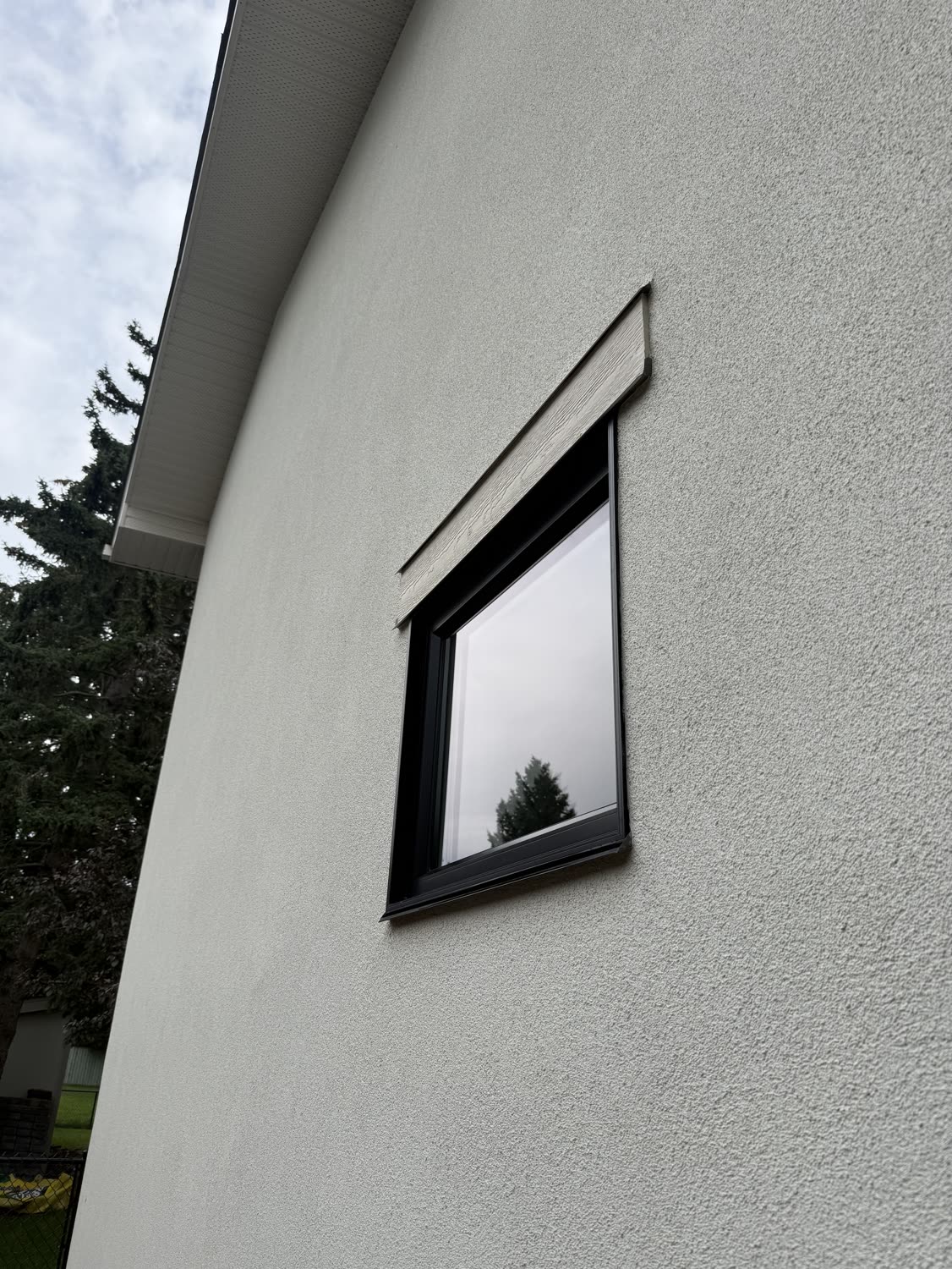 Black-framed window in a stucco wall on a Calgary home, glass clear after an exterior clean and reflecting a spruce