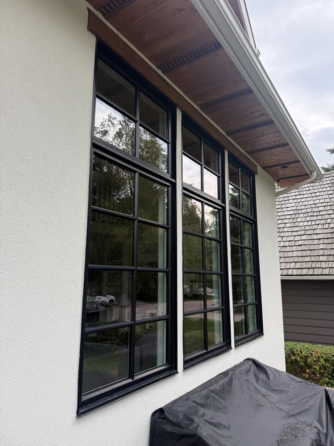 Three tall grid-pane windows with black frames on a white stucco Calgary home after exterior window cleaning